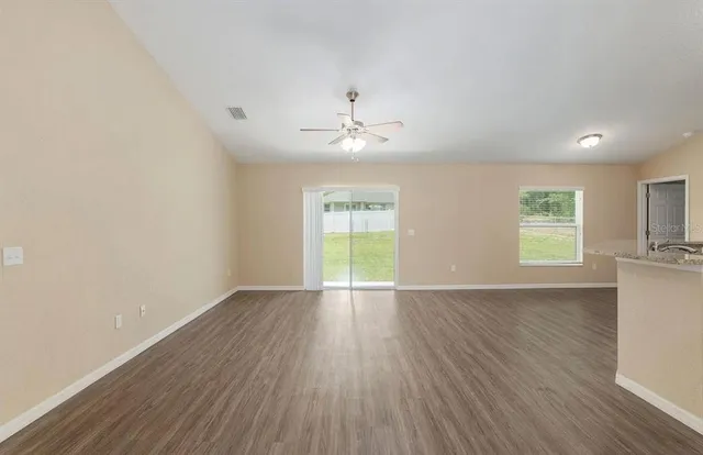 an empty room with wooden floor chandelier fan and windows