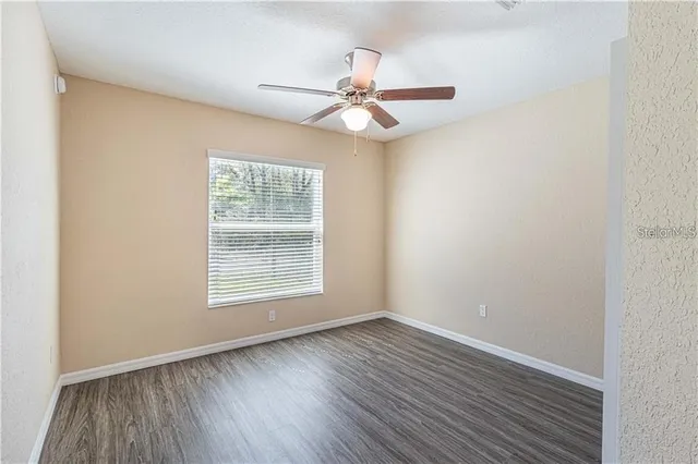 an empty room with wooden floor fan and windows