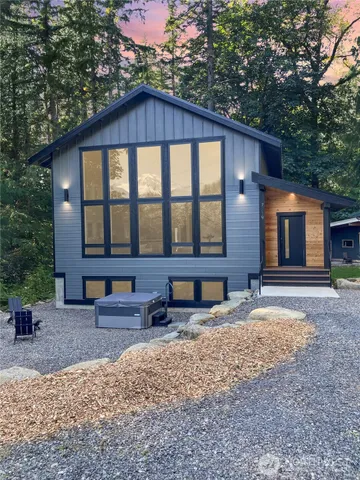 a front view of a house with a yard chairs and large tree
