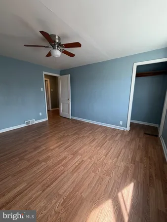 a view of an empty room with wooden floor and a ceiling fan