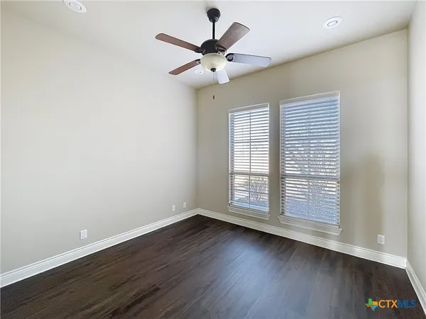 an empty room with wooden floor fan and windows