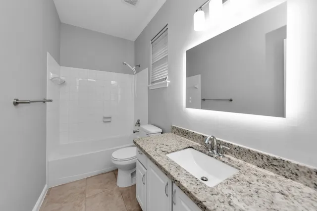 a bathroom with a granite countertop sink a toilet a mirror and shower