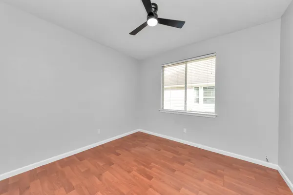 an empty room with wooden floor ceiling fan and windows