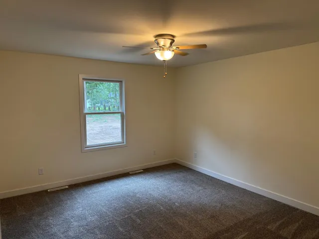an empty room with a chandelier fan and windows