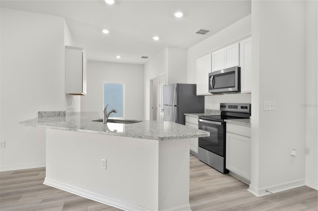 13261 Tula Loop Astatula, FL 34705 - Photo 4 of 25 a kitchen with kitchen island granite countertop a sink stainless steel appliances and white cabinets