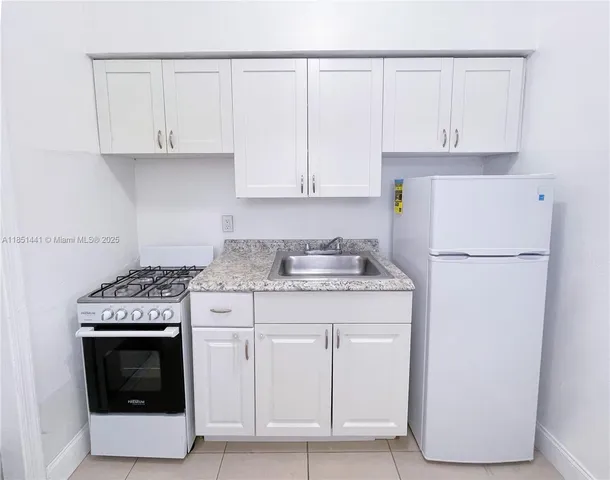 a kitchen with granite countertop white cabinets and refrigerator
