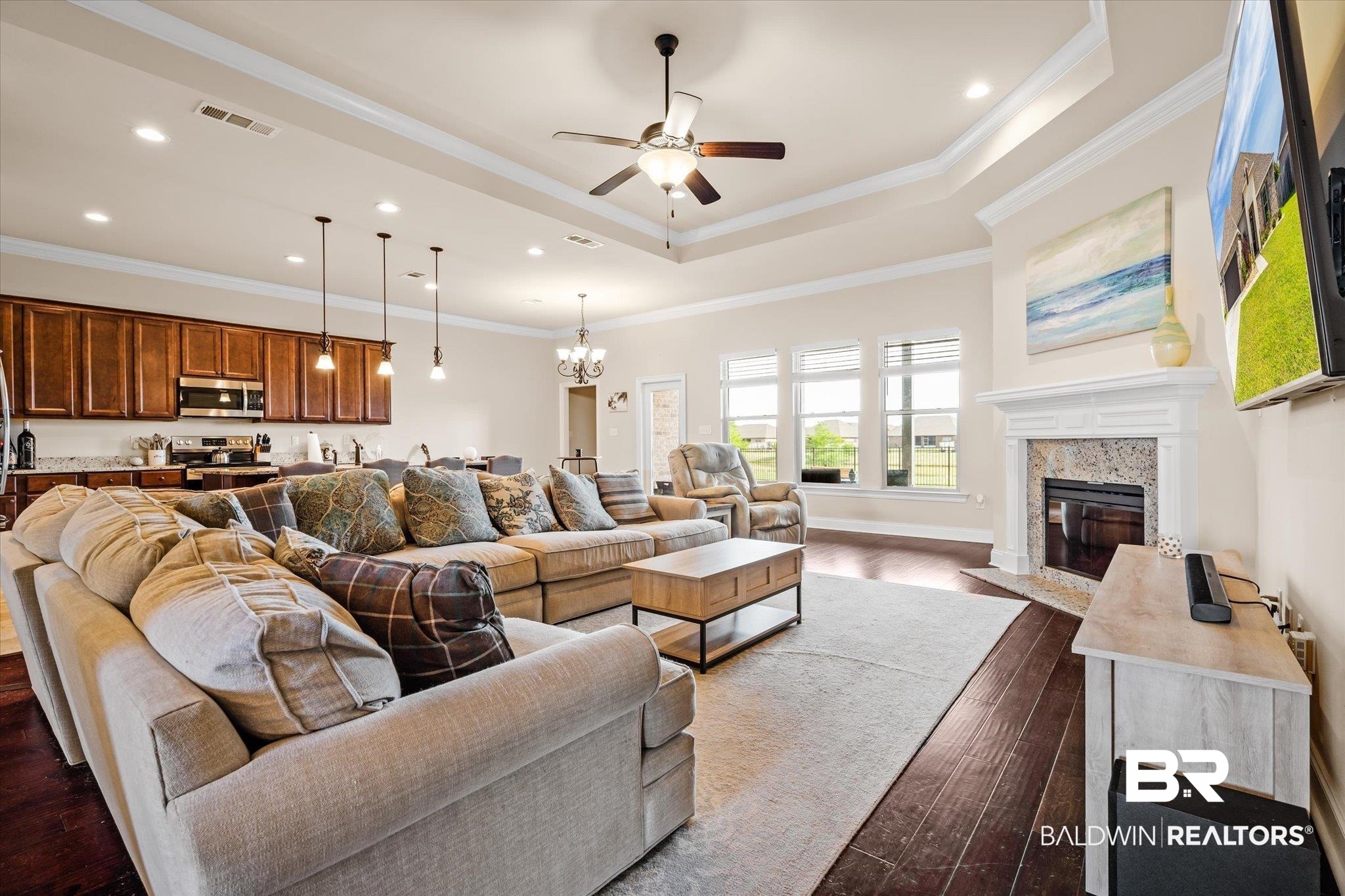 Living area with ceiling fan, crown molding, dark wood-style flooring, a chandelier, and a raised ceiling