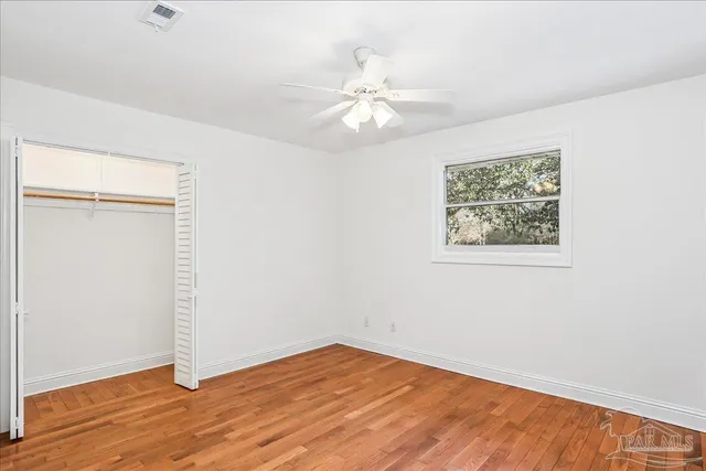a view of an empty room with wooden floor and a ceiling fan