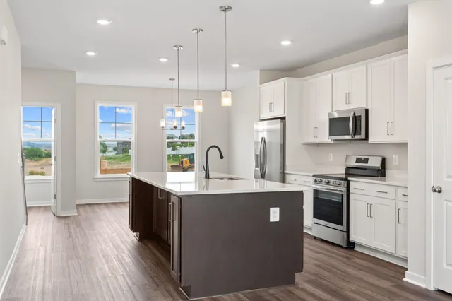 a kitchen with stainless steel appliances granite countertop a stove a sink dishwasher a refrigerator white cabinets and wooden floor next to a window