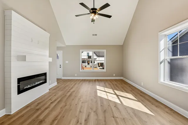 an empty room with wooden floor chandelier fan and windows