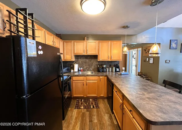 a kitchen with stainless steel appliances kitchen island granite countertop a refrigerator a stove a sink a dining table and chairs with wooden floor