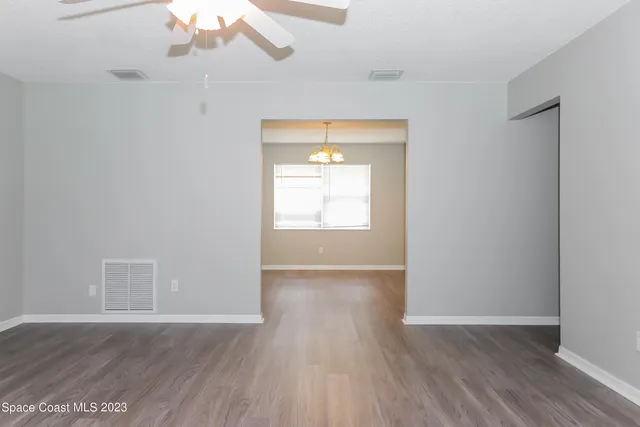 an empty room with wooden floor chandelier and windows