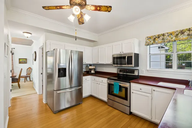 a kitchen with stainless steel appliances a refrigerator a stove top oven a sink dishwasher and white cabinets with wooden floor