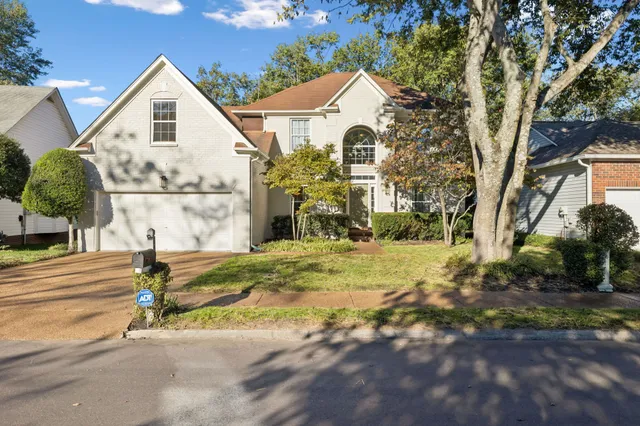 a view of a white house next to a yard with big trees