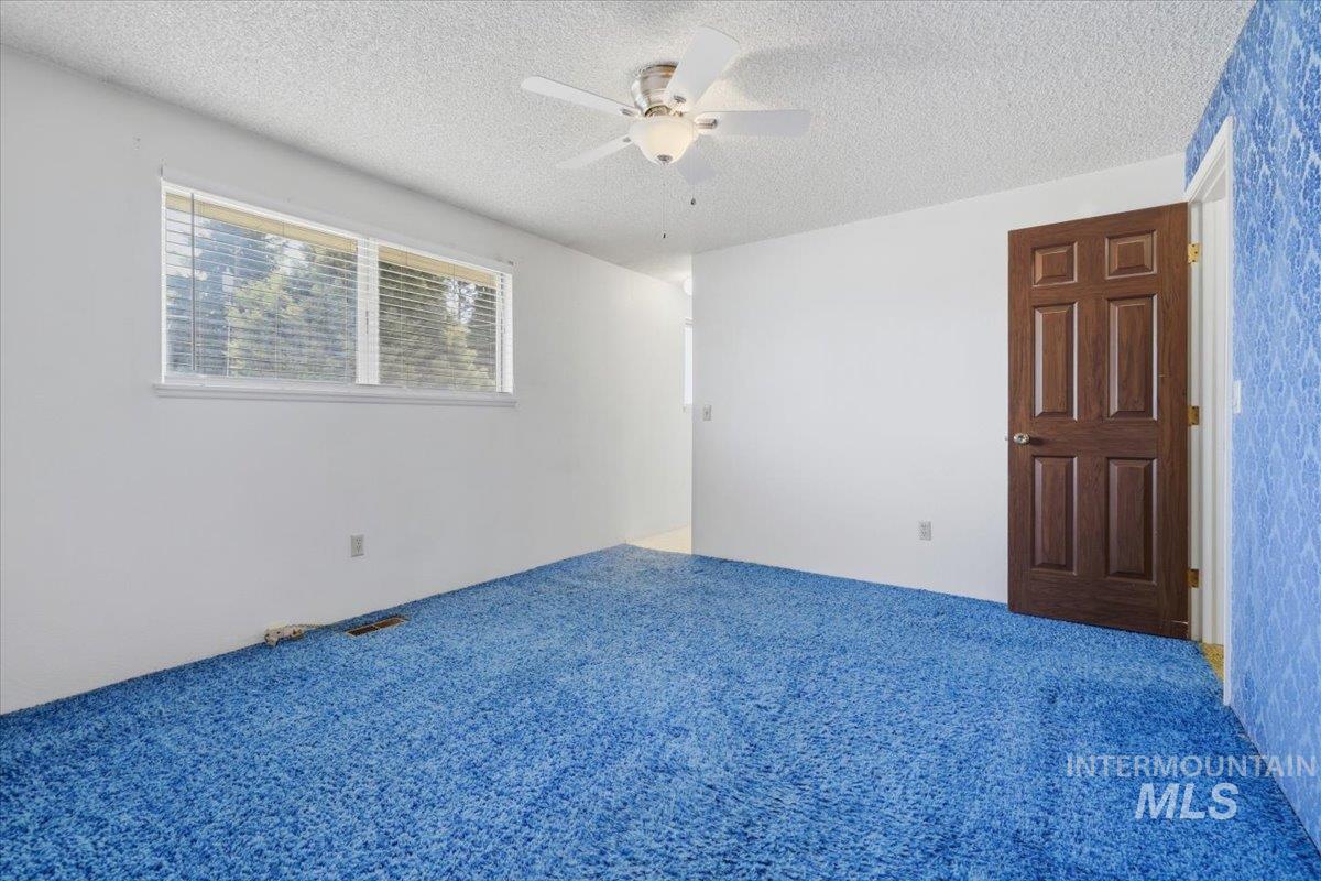 1311 North Middleton Road Nampa, ID 83651 - Photo 26 of 49 Spacious room featuring broadloom carpeting, a multi-pane window with horizontal blinds, a ceiling fan with integrated lighting, a paneled door with a brass-finish knob, and a textured accent wall