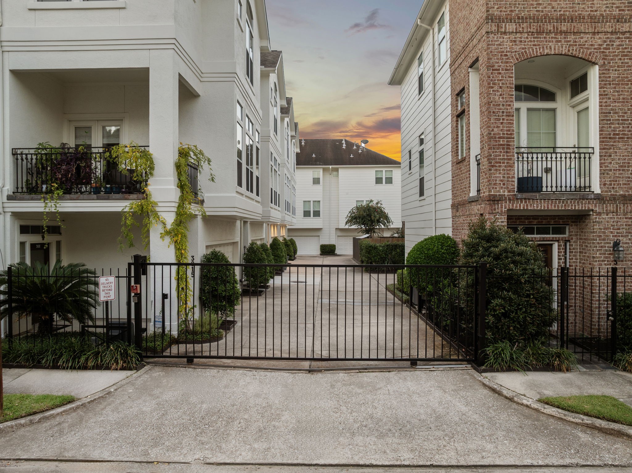 3929 Floyd Street Houston, TX 77007 - Photo 5 of 42 Security gate opens to a manicured driveway surrounded by elegant stucco and brick townhomes, each featuring lush greenery and private balconies. Controlled access enhances privacy and exclusivity, while the low-maintenance grounds offer convenience in a prime Houston location near premier shopping and dining.