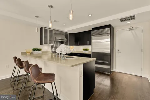 a kitchen with stainless steel appliances kitchen island granite countertop a refrigerator a stove a sink a dining table and chairs with wooden floor