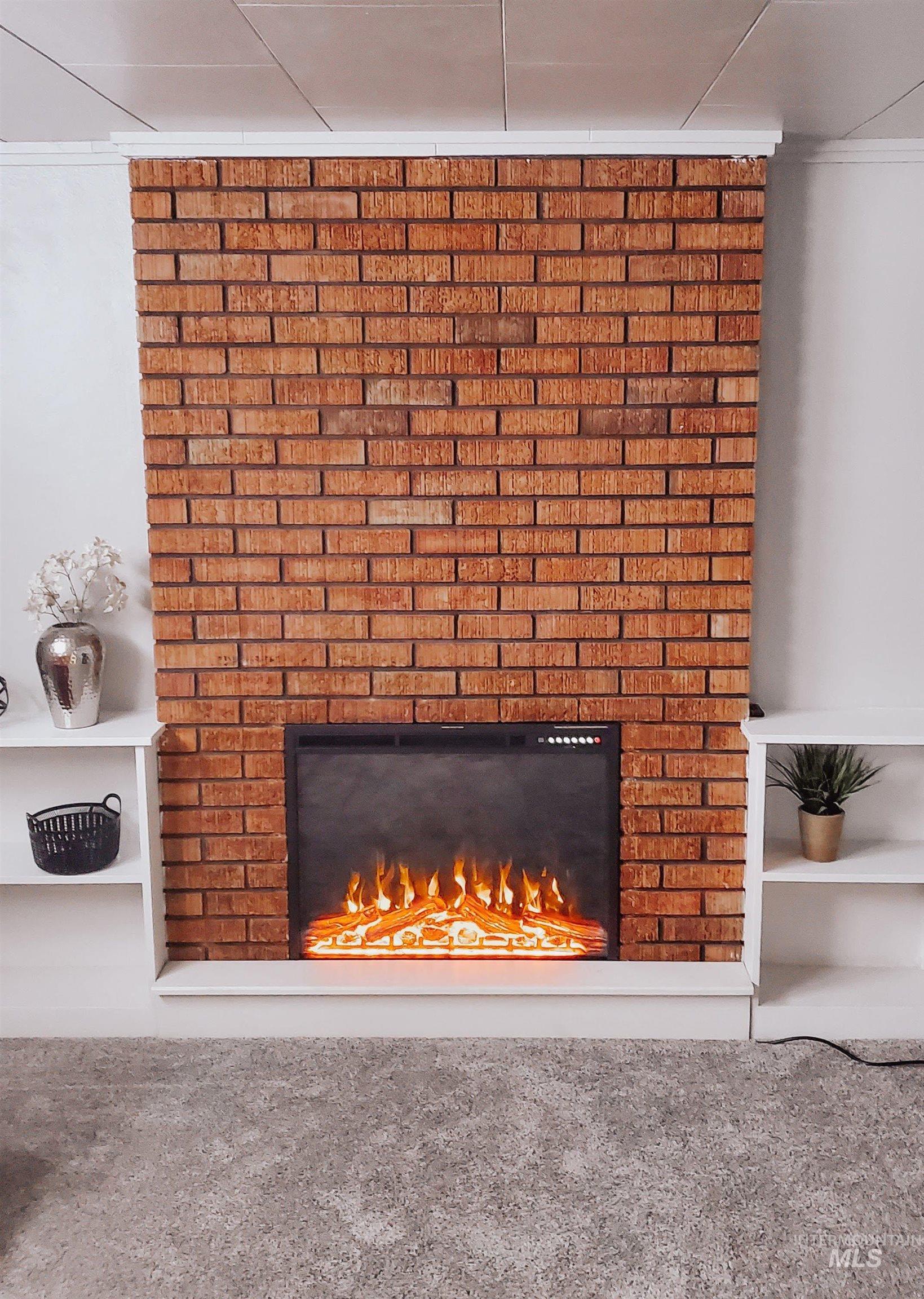 814 Baker Street Boise, ID 83706 - Photo 12 of 26 Exposed brick fireplace surround with an electric insert, flanked by built-in white shelving, above gray carpet flooring