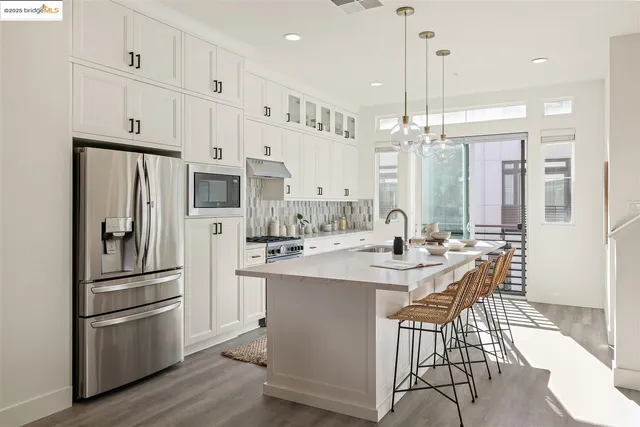 a kitchen with stainless steel appliances a refrigerator a stove a sink and a dining table with wooden floor