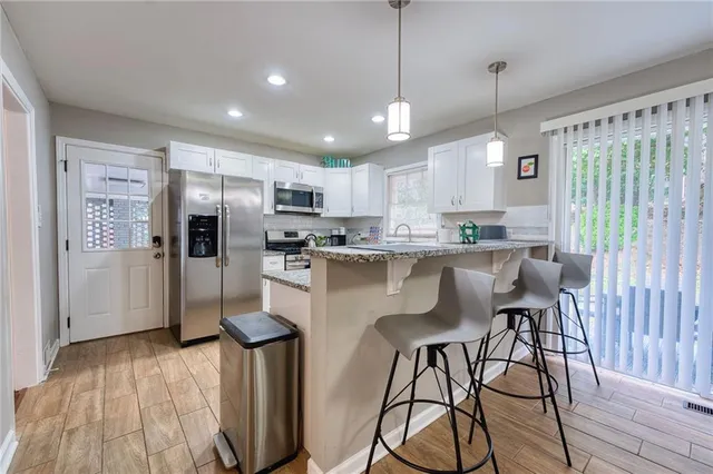 a kitchen with stainless steel appliances granite countertop a refrigerator a sink dishwasher a stove and white cabinets with wooden floor