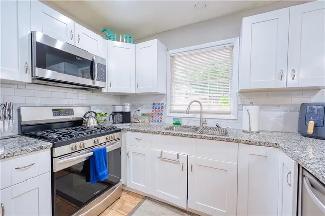 a kitchen with granite countertop white cabinets stainless steel appliances a sink and window