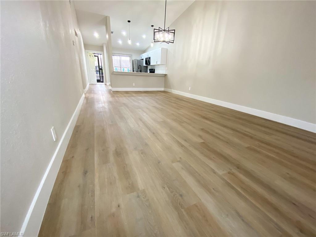 4180 Looking Glass Lane, Unit 4108 Naples, FL 34112 - Photo 20 of 21 Unfurnished living room featuring light wood-type flooring, baseboards, a chandelier, and lofted ceiling