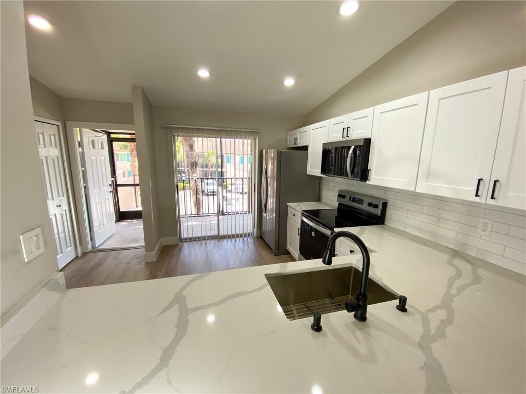 4180 Looking Glass Lane, Unit 4108 Naples, FL 34112 - Photo 3 of 21 Kitchen with stainless steel appliances, white cabinetry, backsplash, and light stone countertops