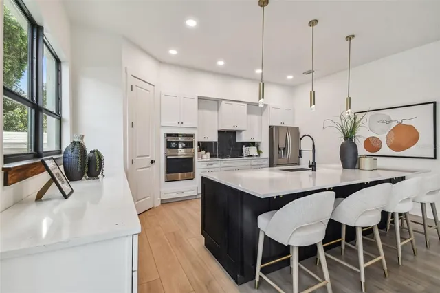 a kitchen with stainless steel appliances kitchen island granite countertop a sink a stove a refrigerator and island with wooden floor