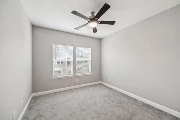 an empty room with ceiling fan and windows