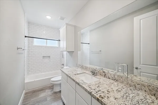 a bathroom with a granite countertop sink a toilet a mirror and shower