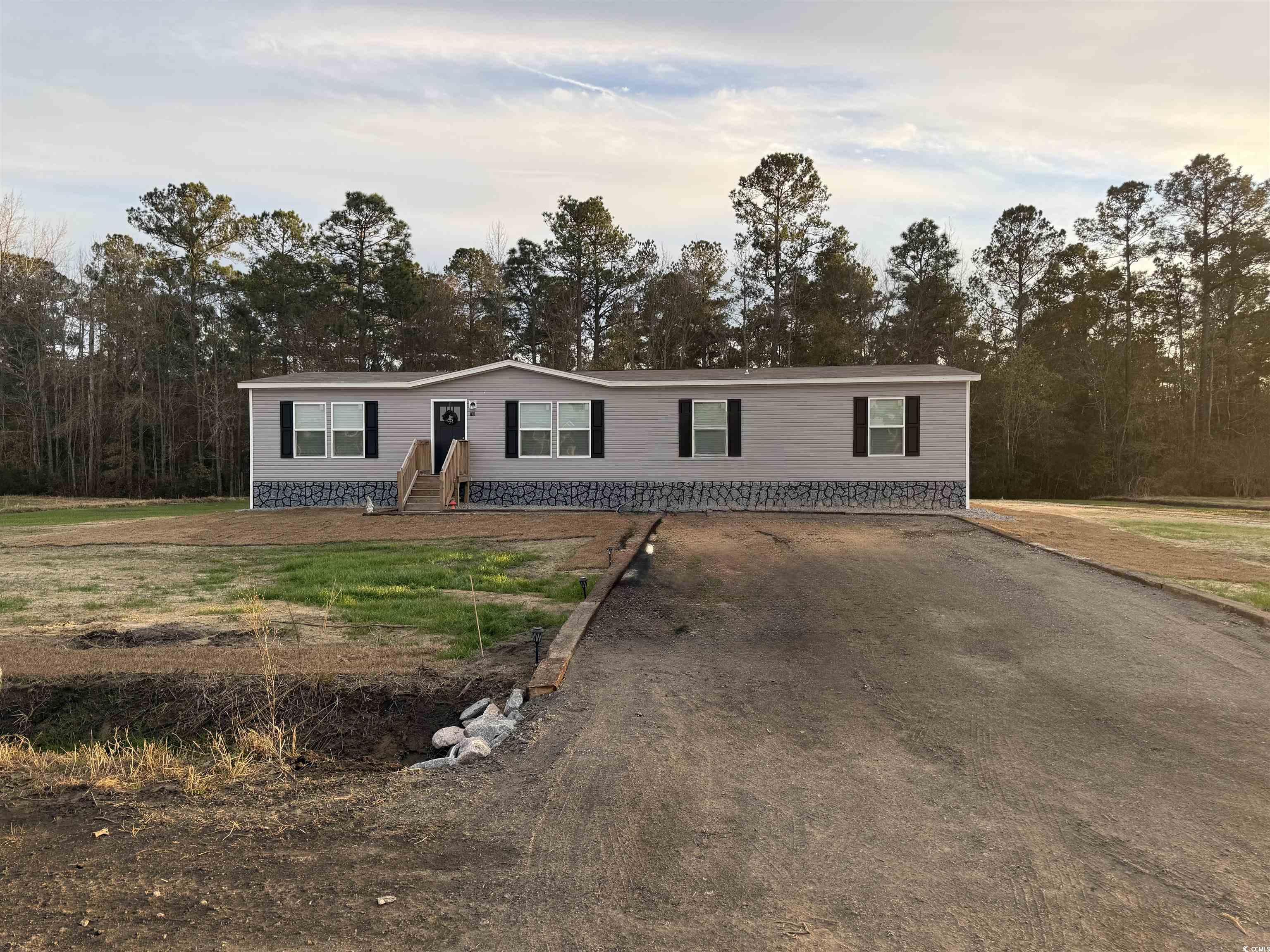 Manufactured / mobile home featuring driveway, a front yard, and view of scattered trees