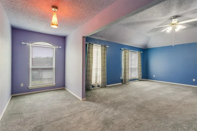 an empty room with chandelier fan and windows