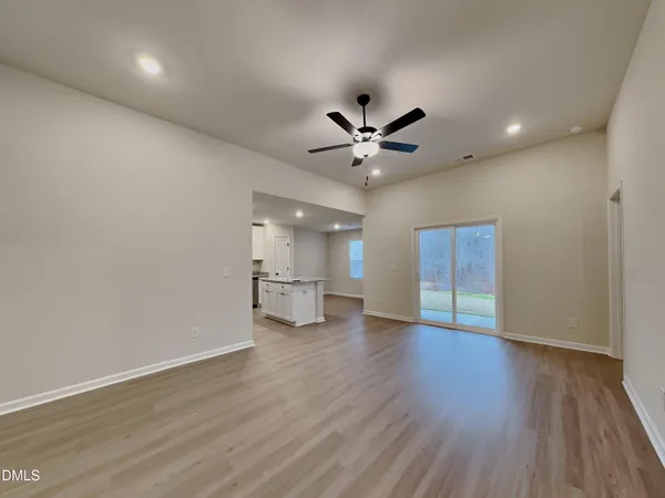 a view of an empty room with wooden floor and a ceiling fan