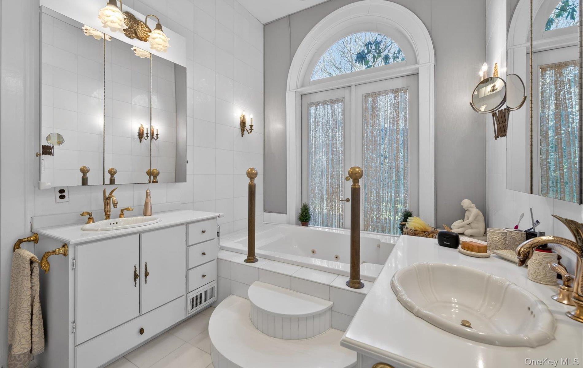 38 Tiffany Road Oyster Bay, NY 11771 - Photo 20 of 50 Primary bath, with two vanities, a Soaking tub, French door opens to view of beautiful gardens healthy amount of natural light, tile walls, and light tile patterned floors.