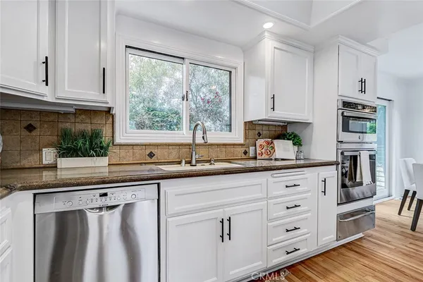a large kitchen with stainless steel appliances kitchen island granite countertop a large stove a sink dishwasher and white cabinets with wooden floor