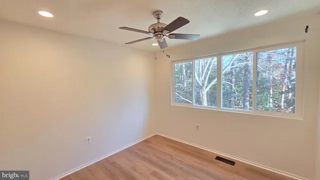 an empty room with wooden floor fan and windows