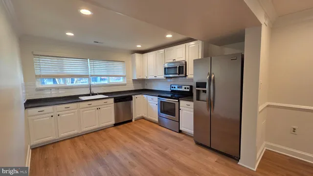 a kitchen with kitchen island granite countertop a refrigerator a sink dishwasher a oven with white cabinets and wooden floor