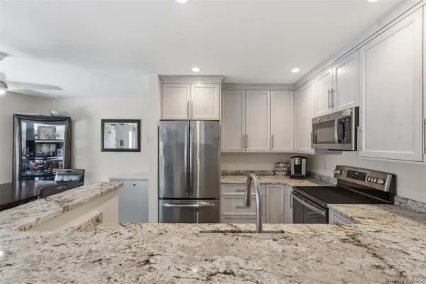 a kitchen with stainless steel appliances granite countertop a refrigerator a stove a sink a refrigerator and white cabinets with wooden floor
