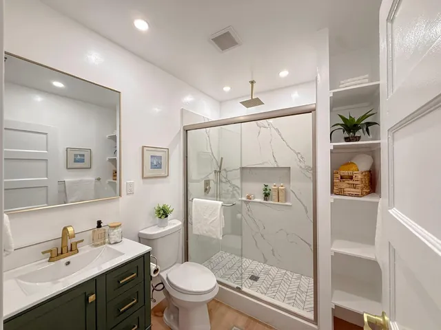 a bathroom with a granite countertop sink a toilet a mirror a vanity and shower
