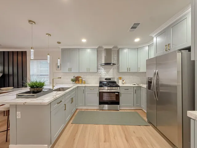 a kitchen with stainless steel appliances granite countertop a refrigerator a sink a stove and white cabinets with wooden floor