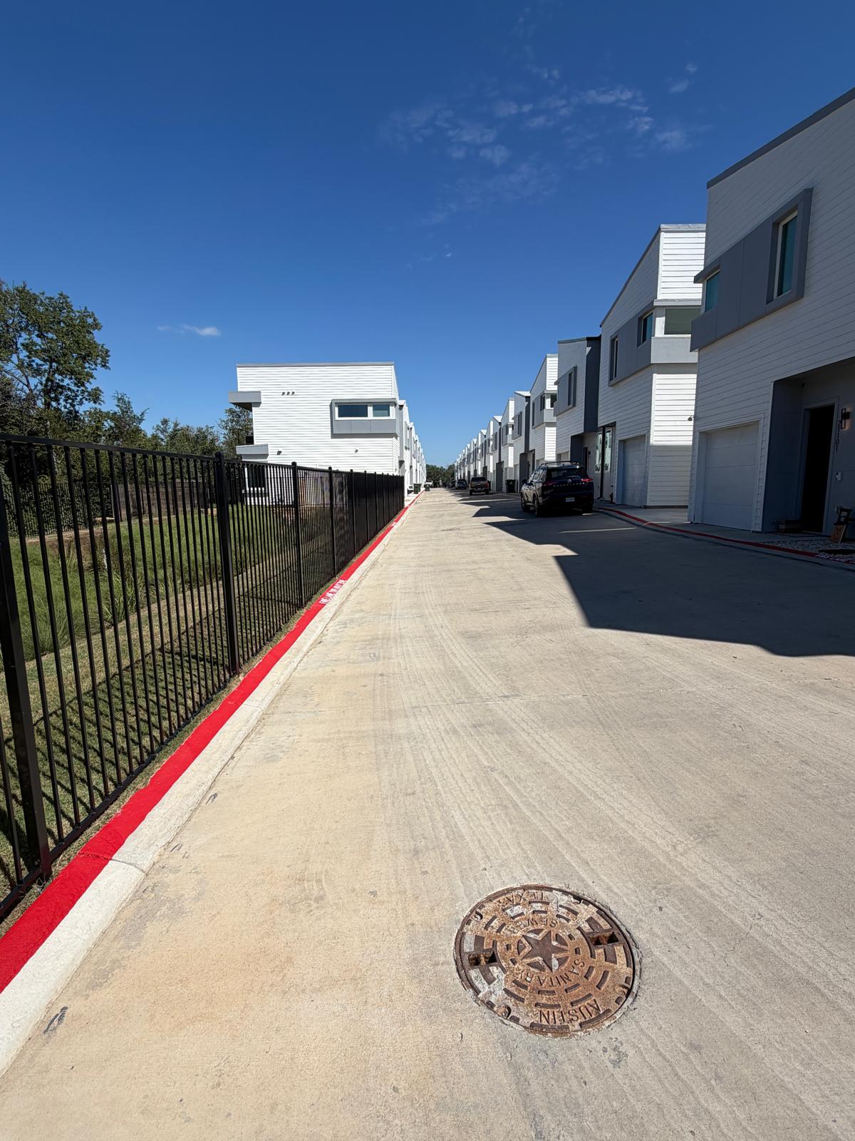 2000 Riverside Farms Road, Unit 12101 Austin, TX 78741 - Photo 4 of 33 Modern multi-level townhomes sit alongside a clean, wide paved driveway under a bright blue sky.
