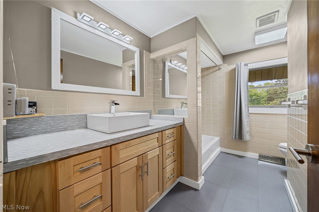 17583 Shurmer Road Strongsville, OH 44136 - Photo 34 of 50 Bathroom featuring a wood-finish vanity with a vessel sink, a large framed mirror, and a tiled shower/tub combination