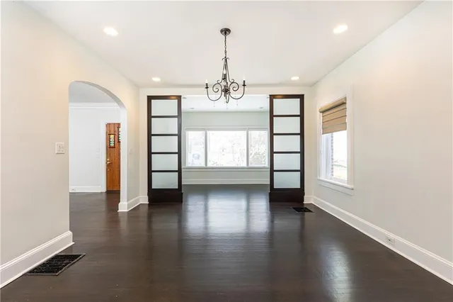 an empty room with wooden floor chandelier and windows