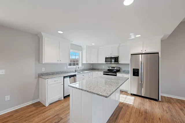 a kitchen with a sink a refrigerator a stove and white cabinets with wooden floor