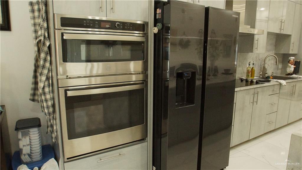 414 Ric Mar Street Edinburg, TX 78541 - Photo 18 of 36 Modern kitchen featuring a built-in stainless steel double oven, a side-by-side refrigerator with an ice and water dispenser, light-toned cabinetry, and a countertop with an integrated sink