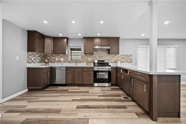 a large kitchen with stainless steel appliances granite countertop a stove a sink dishwasher a refrigerator and white cabinets with wooden floor