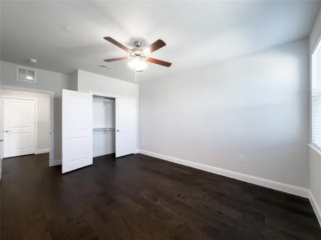 a view of an empty room with wooden floor and a ceiling fan