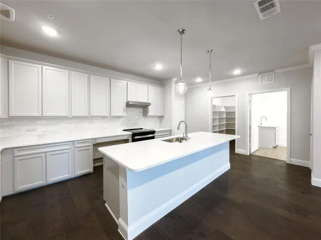 a large white kitchen with kitchen island a sink dishwasher a stove a dining table and chairs with wooden floors