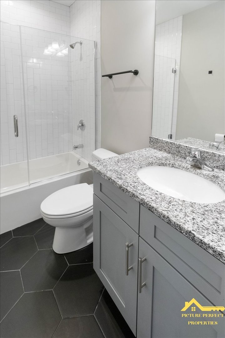 6337 South Ellis Avenue, Unit 3 Chicago, IL 60637 - Photo 7 of 12 a bathroom with a granite countertop sink toilet a mirror and bathtub