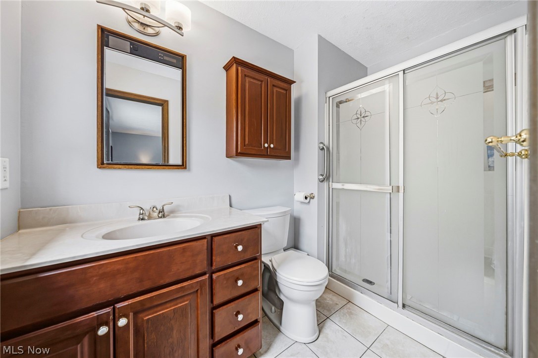 10610 Ridgewater Drive Painesville, OH 44077 - Photo 16 of 23 Bathroom featuring a vanity with a white countertop and wood-finish cabinetry, a framed mirror, a wall-mounted cabinet, a toilet, and a shower with frosted glass doors